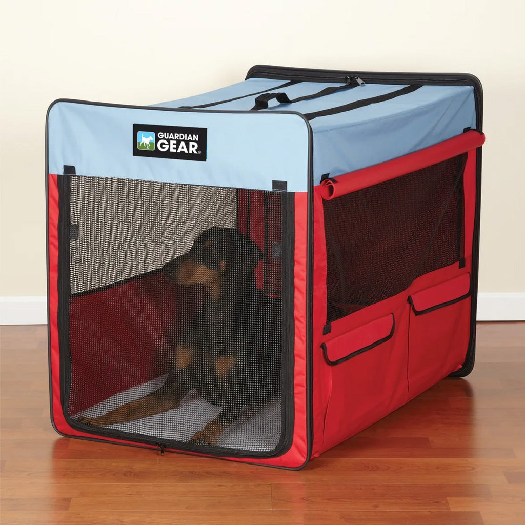 Red and blue pet crate with a dog inside on a wooden floor.