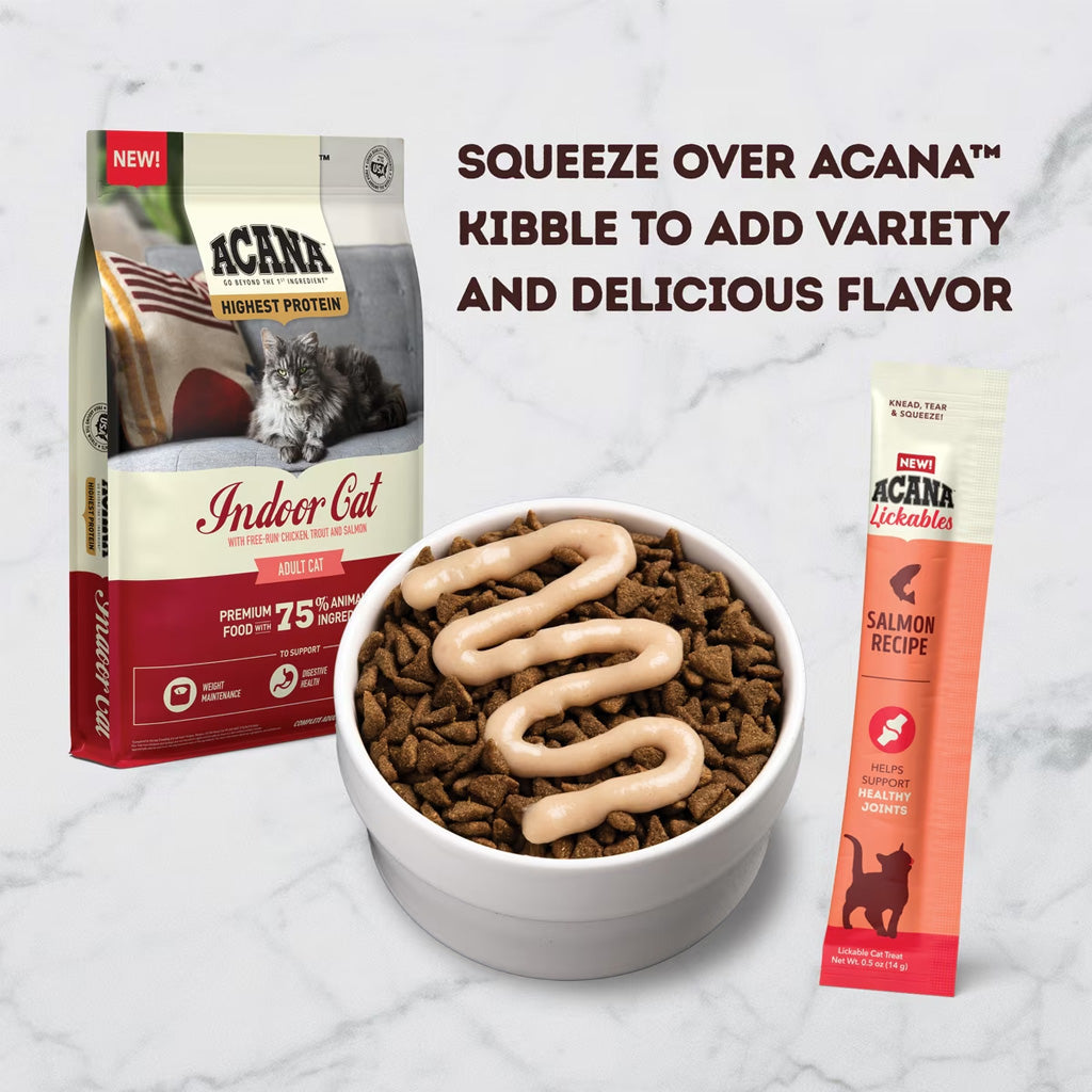 Acana cat food package, bowl with kibble and cream, and a lickable treat on a marble background.