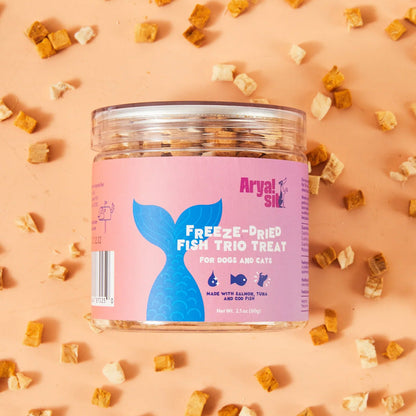 Jar of freeze-dried fish trio treats for dogs and cats on a pink background with scattered treats.