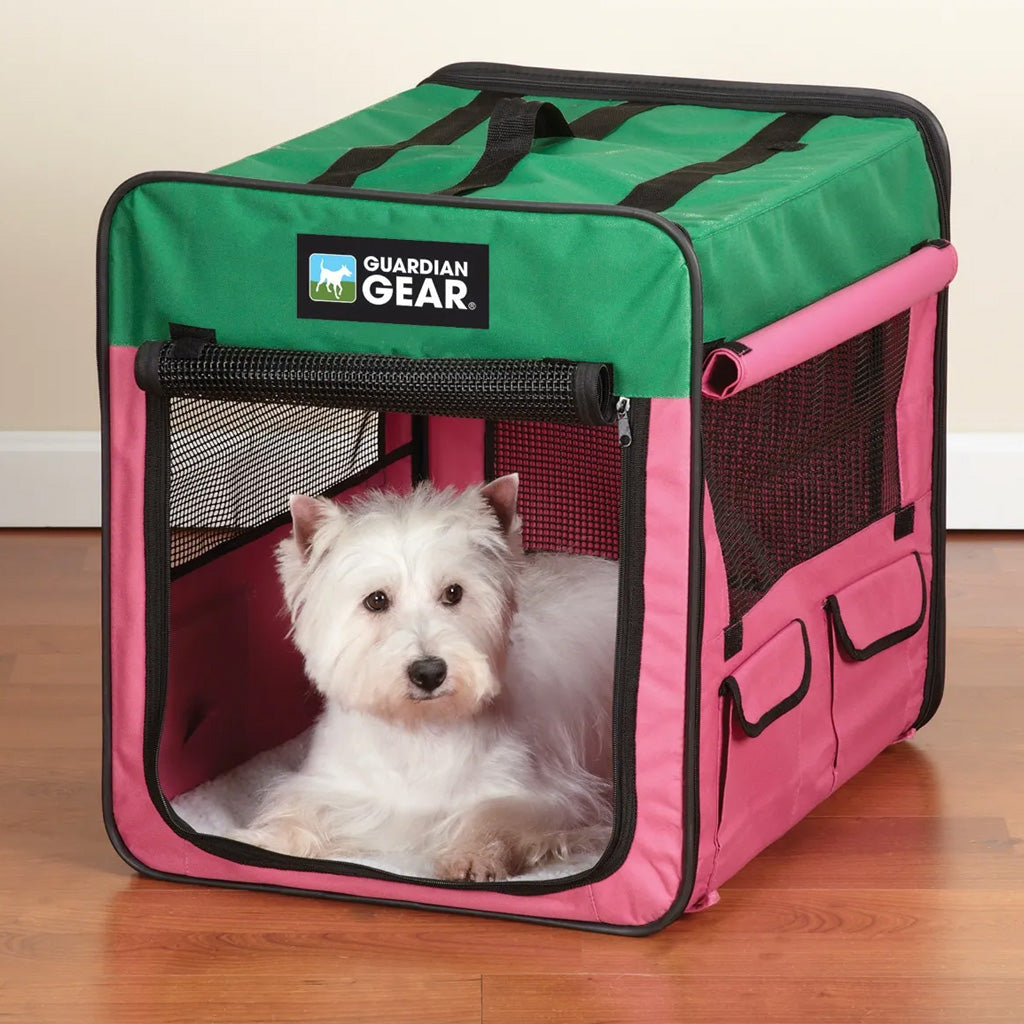 White dog inside a pink and green Guardian Gear pet crate on a wooden floor.