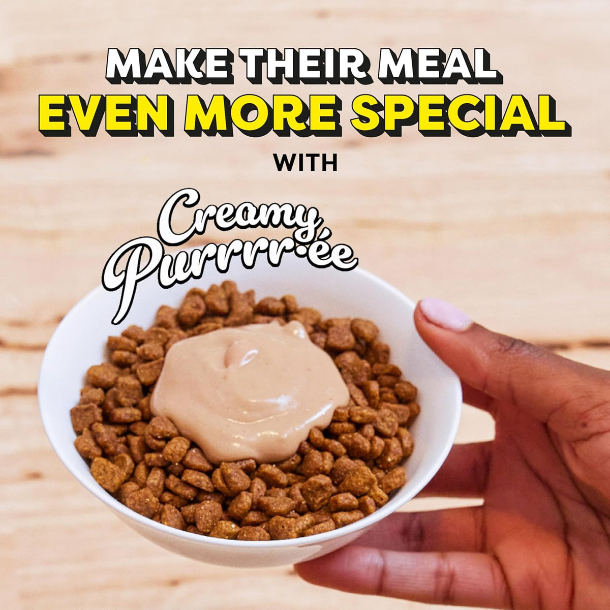 Hand holding a bowl of dog food with creamy purrree on a wooden surface